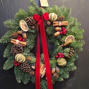 May include: A Christmas wreath featuring evergreen foliage, decorated with pine cones, dried citrus, cinnamon sticks, acorns, and red berries. A bright red ribbon provides a striking contrast. Ideal for festive decoration.