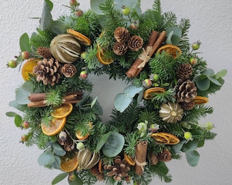 May include: A green Christmas wreath decorated with dried orange slices, cinnamon sticks, pine cones, and eucalyptus leaves.