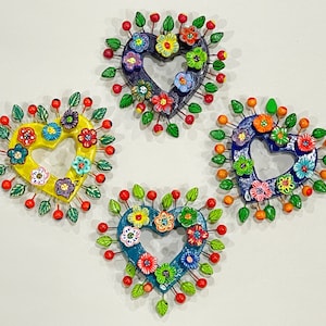 May include: Four colorful heart-shaped ornaments with floral designs and red beads around the edges. The hearts are made of clay and have a rustic, handmade look.