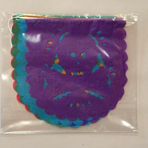 Puede incluir: Un conjunto de recortes de papel de colores en forma de calavera y huesos cruzados. Los recortes est&aacute;n superpuestos y tienen un borde festoneado. Est&aacute;n empaquetados en una bolsa de pl&aacute;stico transparente.