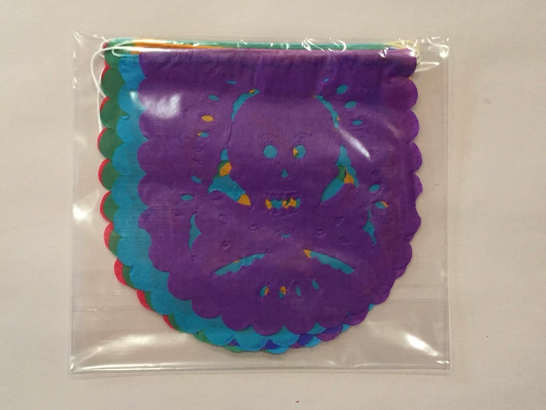 Puede incluir: Un conjunto de recortes de papel de colores en forma de calavera y huesos cruzados. Los recortes est&aacute;n superpuestos y tienen un borde festoneado. Est&aacute;n empaquetados en una bolsa de pl&aacute;stico transparente.