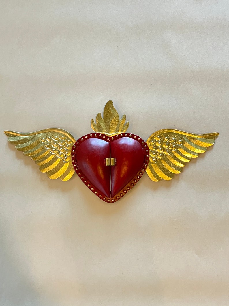 May include: A red heart with gold wings and a flame on top. The heart is decorated with gold studs and has a hinged opening.
