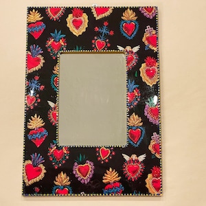 Peut inclure: Un miroir encadré noir avec une bordure décorative de cœurs stylisés colorés. Les cœurs sont rouges, jaunes, bleus et verts avec des accents dorés.
