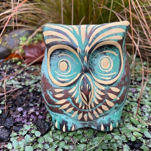 Puede incluir: Una figurita de búho de cerámica azul verdoso con detalles pintados en dorado y marrón. El búho tiene ojos grandes y un diseño detallado en sus plumas.