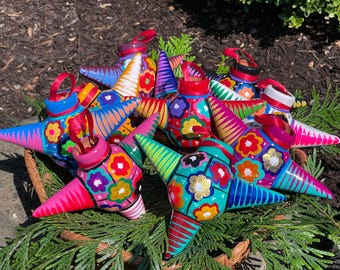 May include: A group of colorful star-shaped pinatas with intricate painted designs. The pinatas are made of papier-mâché and have a variety of colors, including pink, blue, green, yellow, and red. The pinatas are decorated with flowers, stripes, and other patterns.