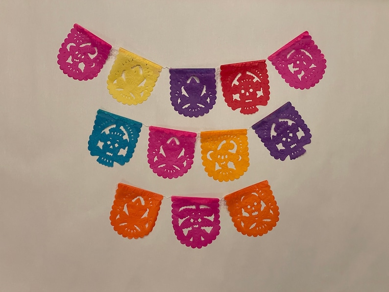Puede incluir: Una guirnalda de papel colorida con tem&aacute;tica del D&iacute;a de Muertos. La guirnalda tiene 10 banderas con intrincados recortes de calaveras y flores en tonos de rosa, morado, azul, amarillo y naranja.
