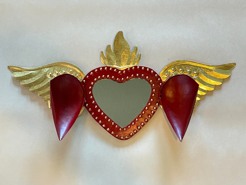 May include: A red heart with gold wings and a mirror in the center. The heart is decorated with gold studs and the wings have a gold leaf finish.