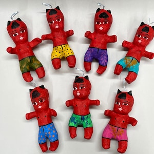 May include: Seven red paper mache dolls with horns and painted faces. Each doll is wearing colorful patterned shorts.