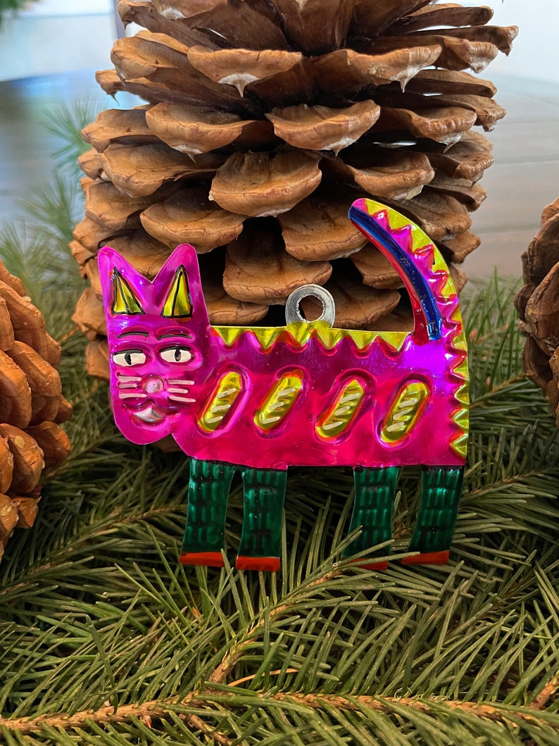 May include: A pink metal cat ornament with green and yellow details. The cat is standing on four legs and has a whimsical design.