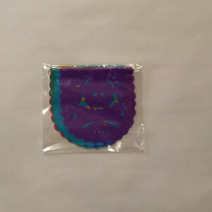 Puede incluir: Un paquete de recortes de papel de colores con un dise&ntilde;o de calavera. Los recortes son en tonos de morado, azul, verde y rojo.