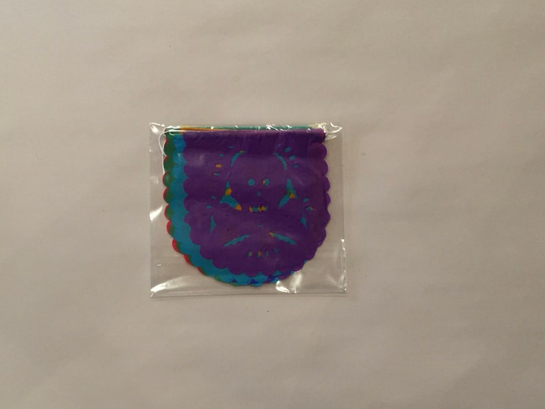 Puede incluir: Un paquete de recortes de papel de colores con un dise&ntilde;o de calavera. Los recortes son en tonos de morado, azul, verde y rojo.