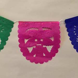 Puede incluir: Una cadena de tres banderines de papel con bordes festoneados. Los banderines son verdes, rosas y azules. Cada bander&iacute;n tiene un dise&ntilde;o recortado de una calavera.