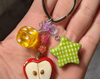 May include: A heart-shaped keychain with a yellow dice, a red apple charm, a green star charm, and pink and purple beads.