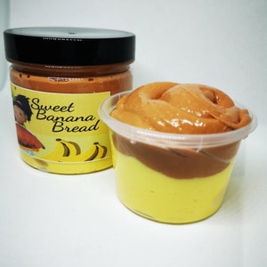 May include: A clear plastic container filled with two layers of brown and yellow slime. The container has a black lid and a label that says "Sweet Banana Bread".