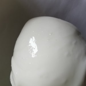 May include: A close-up of a white, smooth, and shiny surface. The surface is slightly textured and has a few small, dark spots.