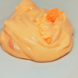 Puede incluir: Primer plano de una slime de color melocot&oacute;n con chispas naranjas en la parte superior. La slime est&aacute; en un plato blanco.