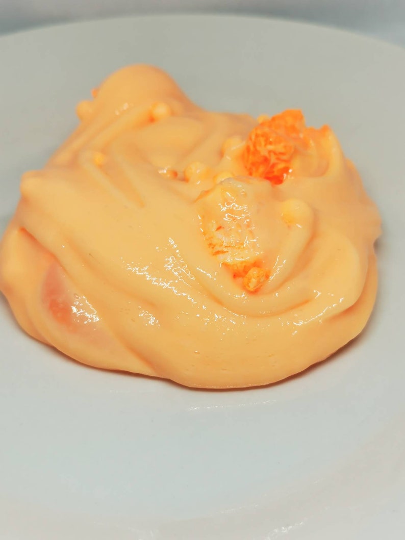 Puede incluir: Primer plano de una slime de color melocot&oacute;n con chispas naranjas en la parte superior. La slime est&aacute; en un plato blanco.