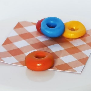 May include: Three mini donuts on a checkered orange and white tablecloth. The donuts are blue, yellow, and orange.