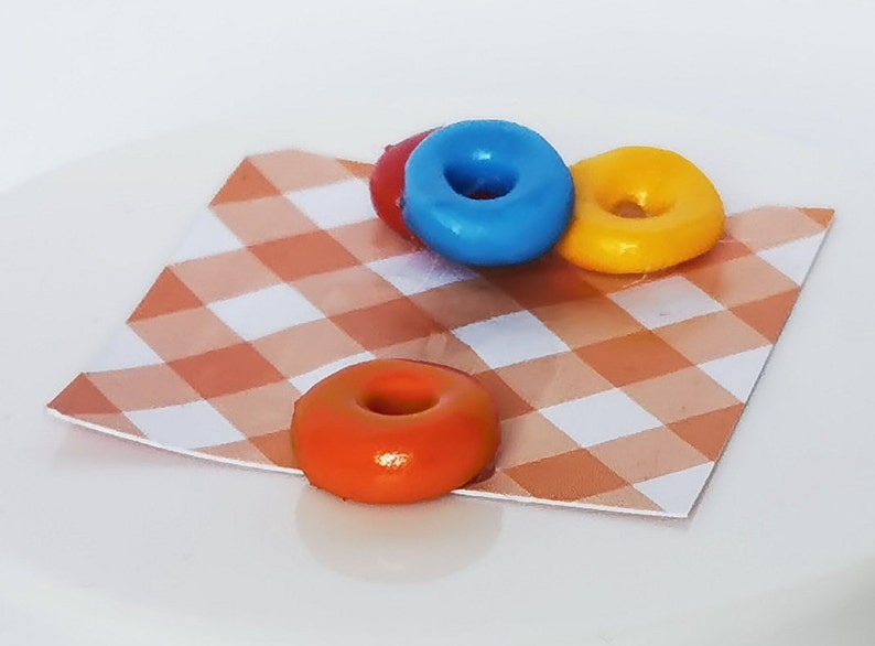 May include: Three mini donuts on a checkered orange and white tablecloth. The donuts are blue, yellow, and orange.