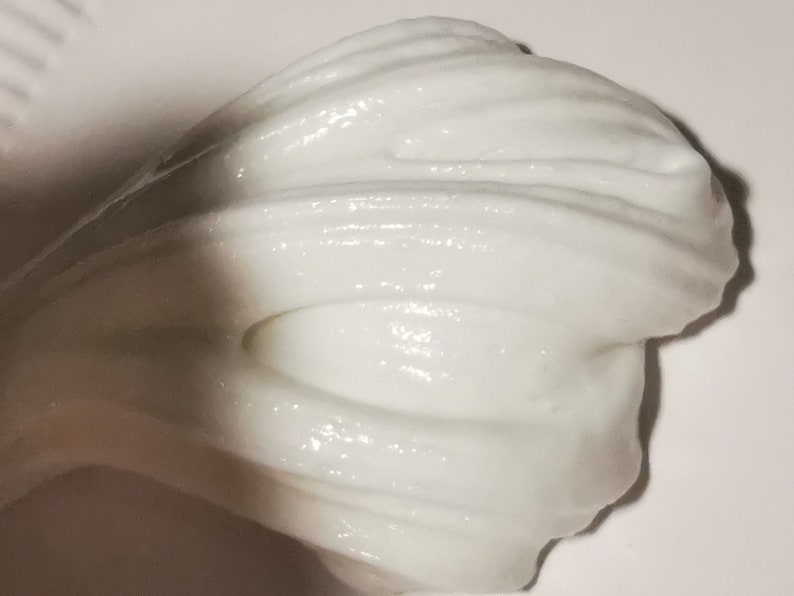 May include: White slime with a smooth, glossy texture. The slime is folded over on itself, creating a wave-like pattern.