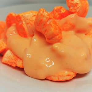Puede incluir: Piezas de cereal inflado de color naranja cubiertas con una salsa cremosa naranja en un plato blanco.