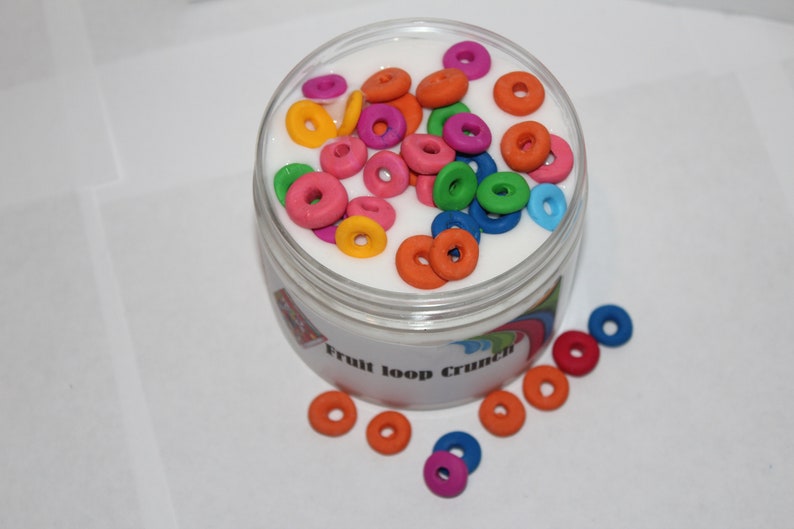 May include: A clear jar filled with white slime and colorful fruit loop shaped charms. The jar has a label that reads "Fruit Loop Crunch".
