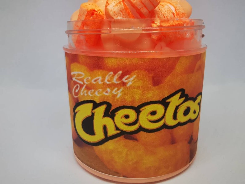 Puede incluir: Un tarro de pl&aacute;stico transparente lleno de slime naranja y blanco con forma de Cheetos. El tarro tiene una etiqueta que dice "Really Cheesy Cheetos".