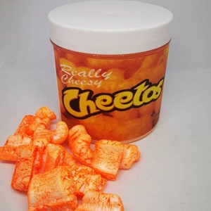 Puede incluir: Un recipiente de pl&aacute;stico blanco con una etiqueta naranja que dice "Really Cheesy Cheetos". El recipiente est&aacute; lleno de palomitas de ma&iacute;z de queso naranja.