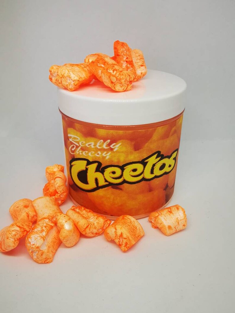 Puede incluir: Snacks de Cheetos de color naranja en un frasco transparente con tapa blanca. El frasco tiene una etiqueta que dice "Really Cheesy Cheetos".