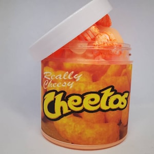Puede incluir: Un tarro transparente con tapa naranja lleno de una baba naranja brillante. El tarro tiene una etiqueta que dice "Really Cheesy Cheetos" con una imagen de Cheetos.