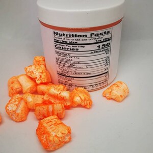 Puede incluir: Un recipiente de pl&aacute;stico blanco con una etiqueta naranja que dice "Nutrition Facts". La etiqueta enumera la informaci&oacute;n nutricional para una porci&oacute;n de 1 oz (28 g). El recipiente est&aacute; lleno de piezas de cereal inflado naranja.
