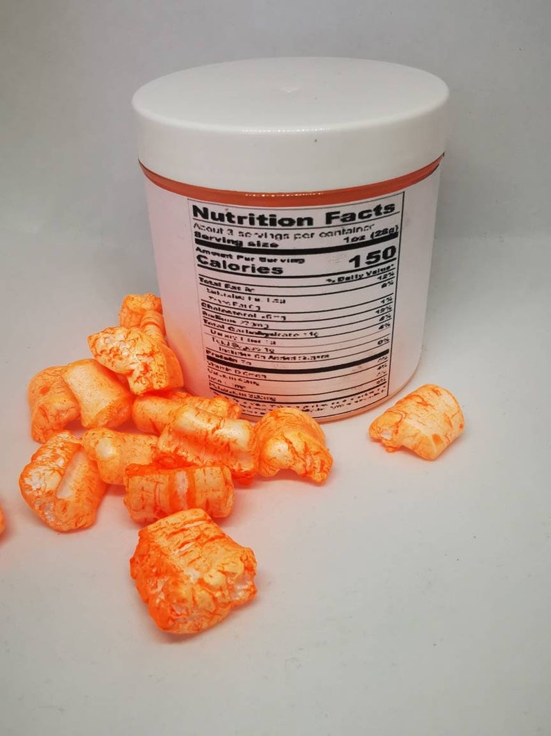 Puede incluir: Un recipiente de pl&aacute;stico blanco con una etiqueta naranja que dice "Nutrition Facts". La etiqueta enumera la informaci&oacute;n nutricional para una porci&oacute;n de 1 oz (28 g). El recipiente est&aacute; lleno de piezas de cereal inflado naranja.