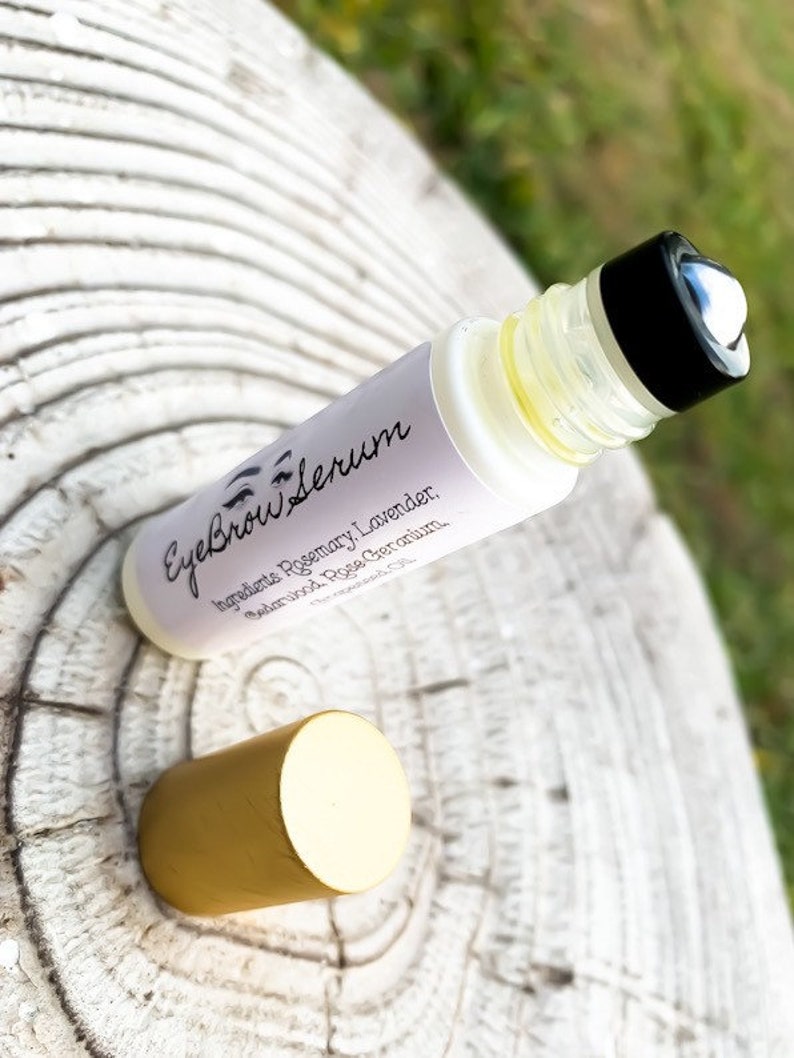Puede incluir: Un frasco de vidrio transparente con tapa negra y tapa dorada. El frasco est&aacute; etiquetado como "Eyebrow Serum" y enumera los ingredientes: Romero, Lavanda, S&aacute;ndalo, Rosa, Geranio.
