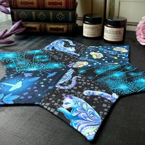 Könnte beinhalten: Ein sternförmiger blauer und schwarzer Stoffuntersetzer mit einem fantasievollen Design mit Eulen, Katzen und löwenzahnartig Mustern. Der Untersetzer ist aus Patchwork-Stoff gefertigt und hat einen dunklen Hintergrund.