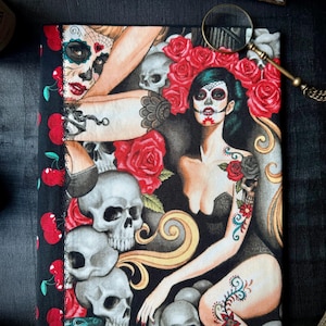 Könnte beinhalten: Ein schwarzer Stoff-Journal-Umschlag mit einem farbenfrohen Design, das zwei Frauen mit Zucker Schädel Make-up, roten Rosen und Schädeln zeigt. Der Stoff hat ein Kirschmuster an der Seite.