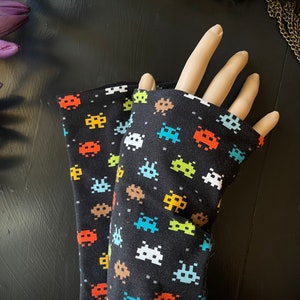 Könnte beinhalten: Ein Paar schwarze Armwärmer mit einem sich wiederholenden Muster aus bunten, pixeligen Space Invaders.
