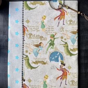 Könnte beinhalten: Eine beige Stofftasche mit Peter-Pan-Motiv. Die Tasche zeigt ein sich wiederholendes Muster von Peter Pan, Tinkerbell, Captain Hook und dem Krokodil. Die Tasche hat einen Reißverschluss und ein blaues und weißes Sternenmuster an der Seite. Der Text "All you need is faith, trust, and a little Pixie Dust." wiederholt sich auf der gesamten Tasche.