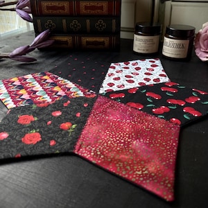 Könnte beinhalten: Ein sternförmiger Patchwork-Tischläufer mit sechs verschiedenen Stoffbahnen. Die Bahnen zeigen verschiedene Muster, darunter rote und weiße Punkte, rote und schwarze Kirschen, rote und weiße Marienkäfer und rote und schwarze Blumenmuster.