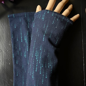 Könnte beinhalten: Ein Paar dunkelblaue Armwärmer mit einem Muster aus türkisfarbenem Binärcode.