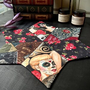 Könnte beinhalten: Ein schwarzer und roter Patchwork-Stoffuntersetzer in Sternform. Der Untersetzer zeigt einen Schädel, Blumen und eine Frau mit Zucker Schädel Make-up. Der Text "Witchcraft Hour" ist auf dem Untersetzer sichtbar.