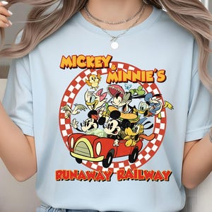 May include: Light blue t-shirt featuring a colorful graphic of Mickey and Minnie Mouse with other Disney characters in a red car. The text "Mickey & Minnie's Runaway Railway" is printed above and below the image.