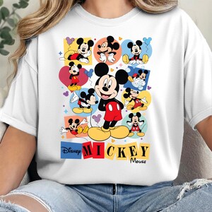 Pu&ograve; includere: T-shirt bianca con una grafica colorata di Mickey Mouse. Il design include pi&ugrave; immagini di Mickey in varie pose, su sfondi colorati. I loghi Disney e Mickey Mouse sono visualizzati in basso.