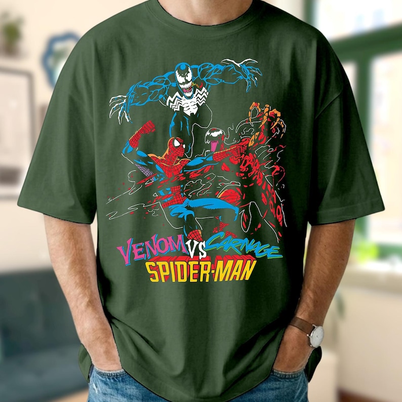 May include: Dark green t-shirt with a vibrant graphic of Venom, Carnage, and Spider-Man. The design features the text "Venom vs Carnage Spider-Man" in a multi-coloured font. The shirt is made of a soft material.