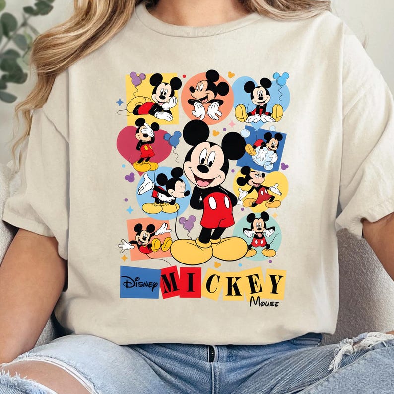 Pu&ograve; includere: T-shirt beige con una grafica colorata di Mickey Mouse. Il design include pi&ugrave; immagini di Mickey in varie pose, su uno sfondo di cuori, quadrati e cerchi. Le parole "Disney MICKEY Mouse" sono stampate in basso.