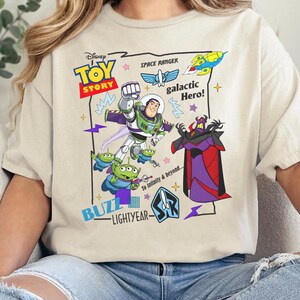 May include: A cream-colored t-shirt featuring a Toy Story graphic with Buzz Lightyear, Zurg, and green aliens. The design includes the text Disney Toy Story, Space Ranger, galactic Hero!, Buzz Lightyear, and To Infinity & beyond... with colorful stars and lightning bolt accents.