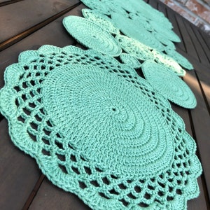 May include: A set of five crocheted doilies in a light green color. The doilies are arranged in a row on a wooden surface.
