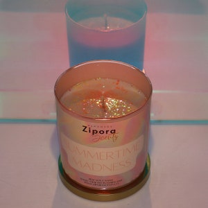 May include: A pink and white candle with gold glitter and the text "Handmade Zipora Scents Summertime Madness 8oz Soy Candle Hand-Crafted in Maryland www.ziporascents.co"