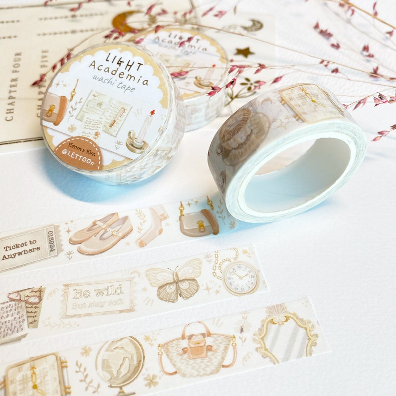 Peut inclure: Trois rouleaux de ruban adh&eacute;sif washi d&eacute;coratif sur fond bleu clair avec des illustrations d'un papillon, d'une horloge, d'un sac &agrave; main, d'un globe terrestre, de chaussures et d'un livre. Le ruban est &eacute;tiquet&eacute; "LIGHT Academia washi tape" et "15mm x 10m @LETTOON".