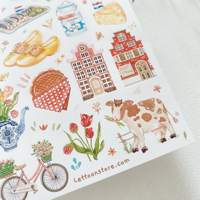 May include: A sheet of stickers featuring illustrations of Dutch culture, including a red brick building, a cow, a bicycle, tulips, and a waffle. The stickers are on a white background and have a whimsical, hand-drawn style.