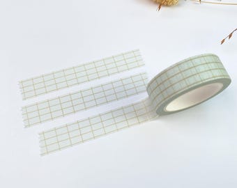 May include: A roll of light green washi tape with a thin gold grid pattern. The tape is partially unrolled, showing two strips extending from the main roll, each featuring the same consistent square grid design on a pale green background.